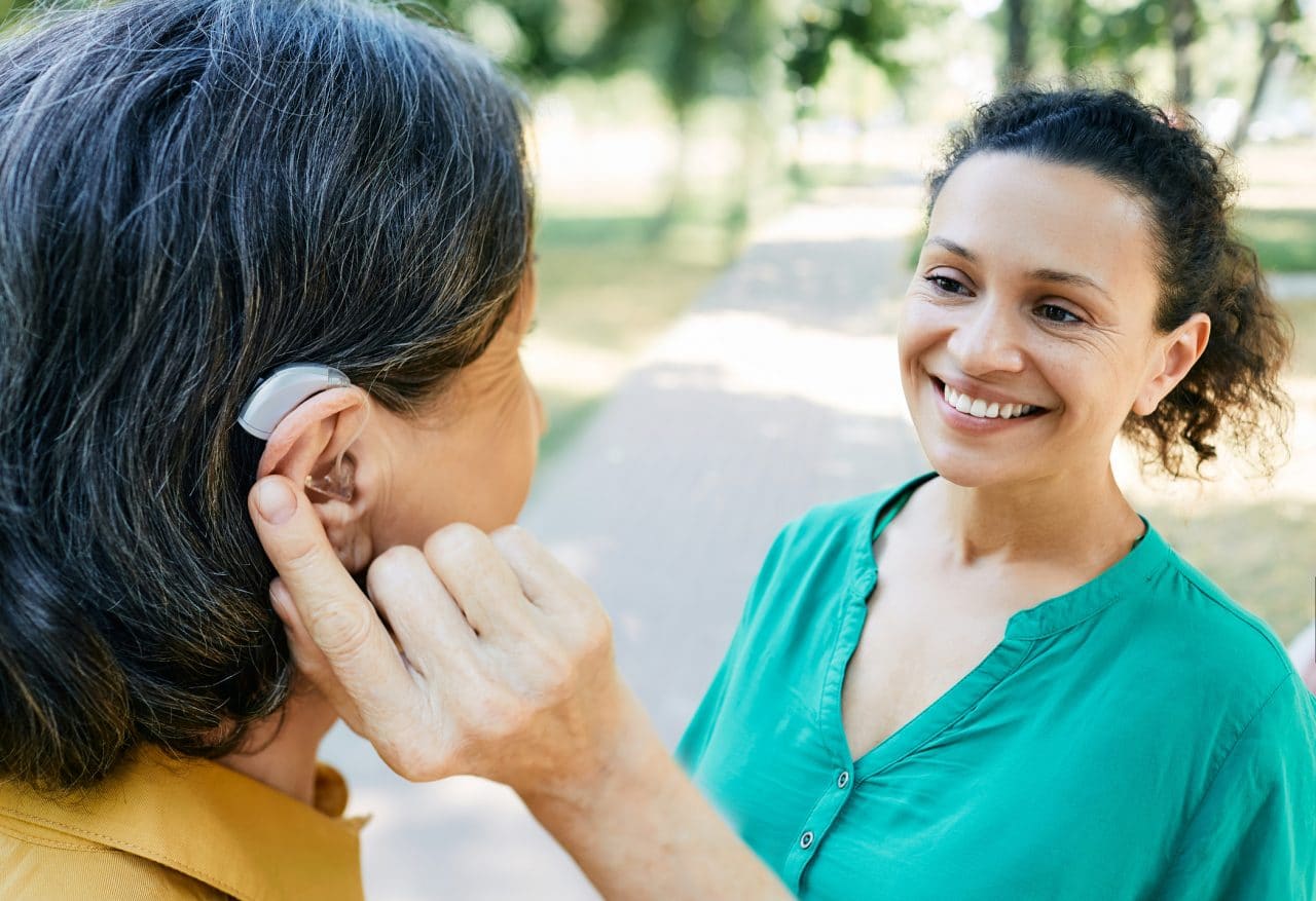 Woman with hearing aid talking to her friend outdoors.