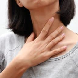 Closeup of a woman with laryngitis touching her hand to her throat.