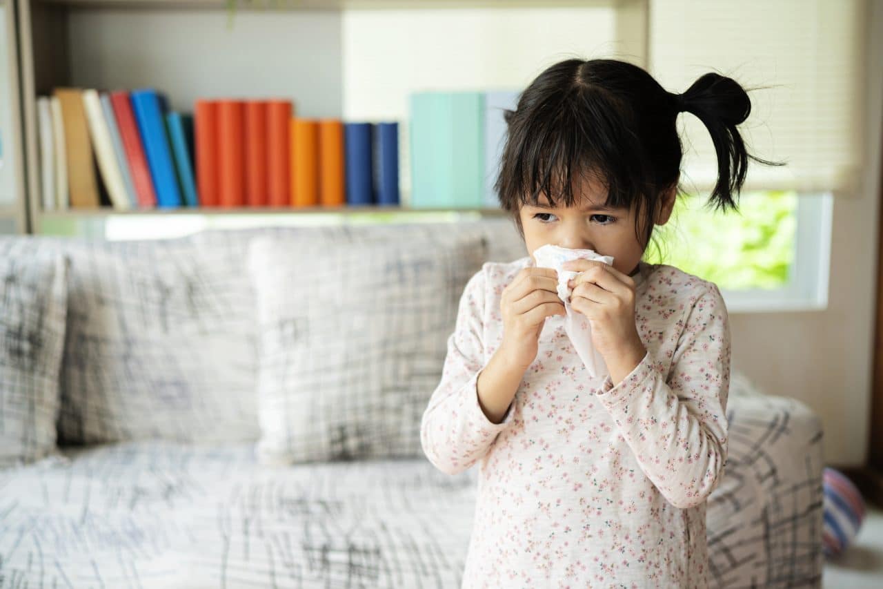 Little girl with a sinus infection wipes her nose with a tissue.