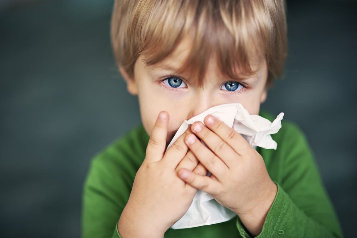 Young boy holds tissue to nose

