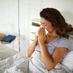 Woman lying in bed blowing her nose into a tissue