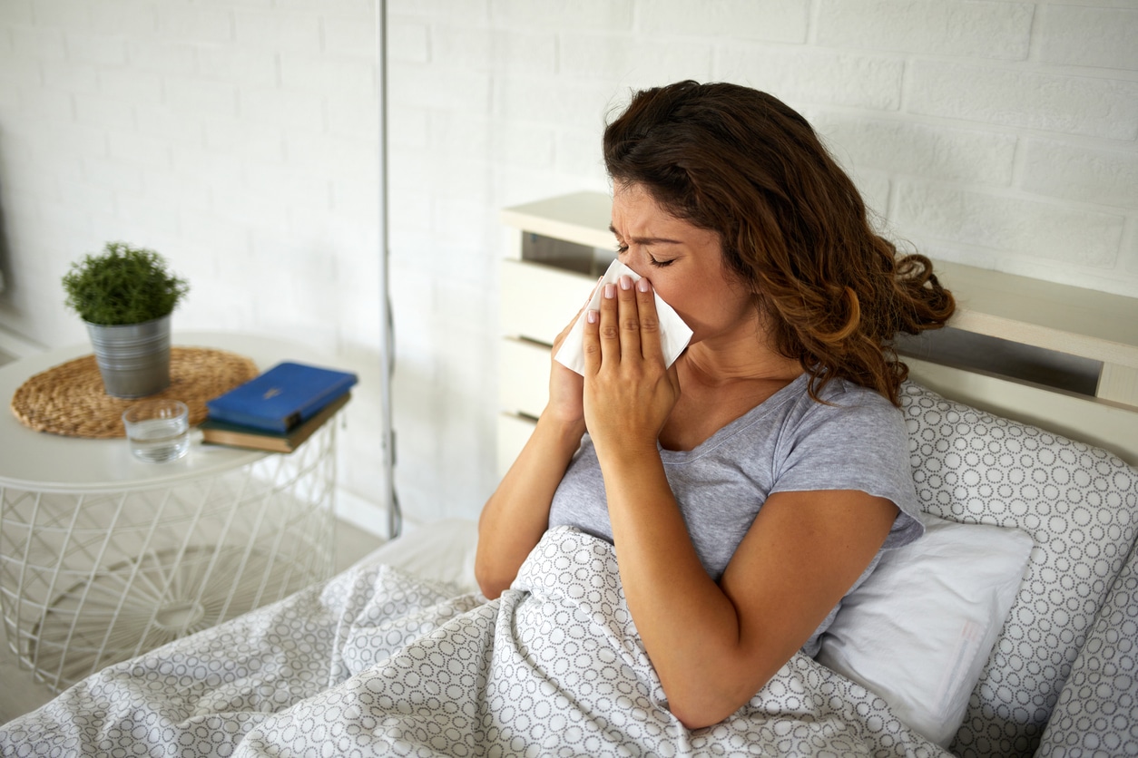 Woman lying in bed blowing her nose into a tissue.