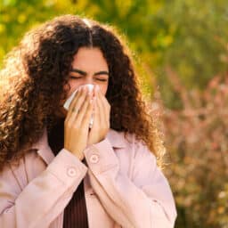 Woman with allergies blowing her nose outside