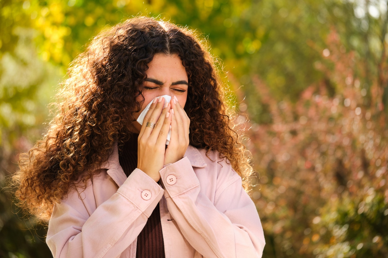 Woman with allergies blowing her nose outside.